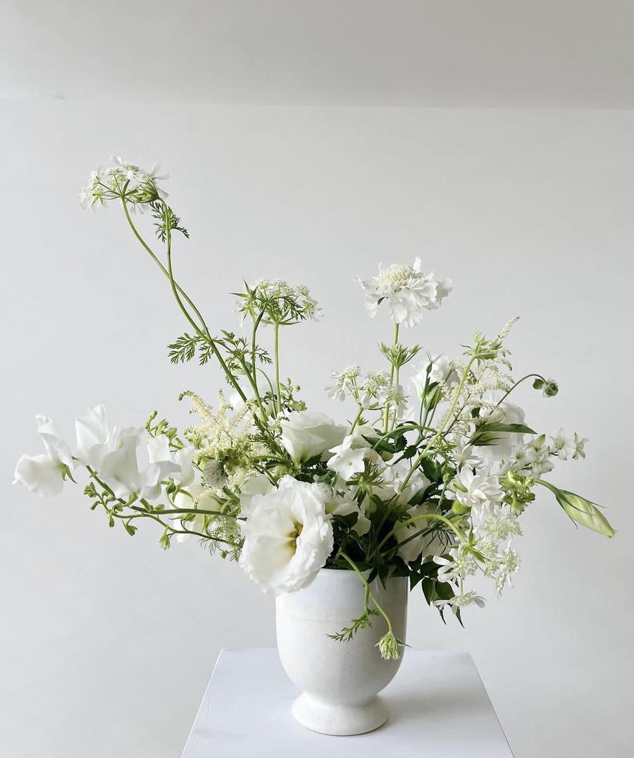 White garden-style arrangement with sweet peas and lisianthus in a stone urn