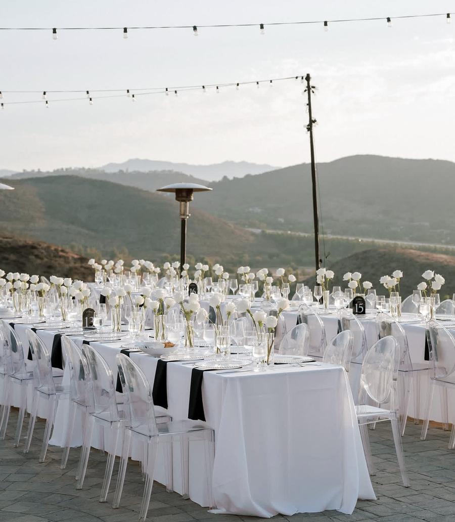 Long white tables with black napkins and white rose bud vases outdoors
