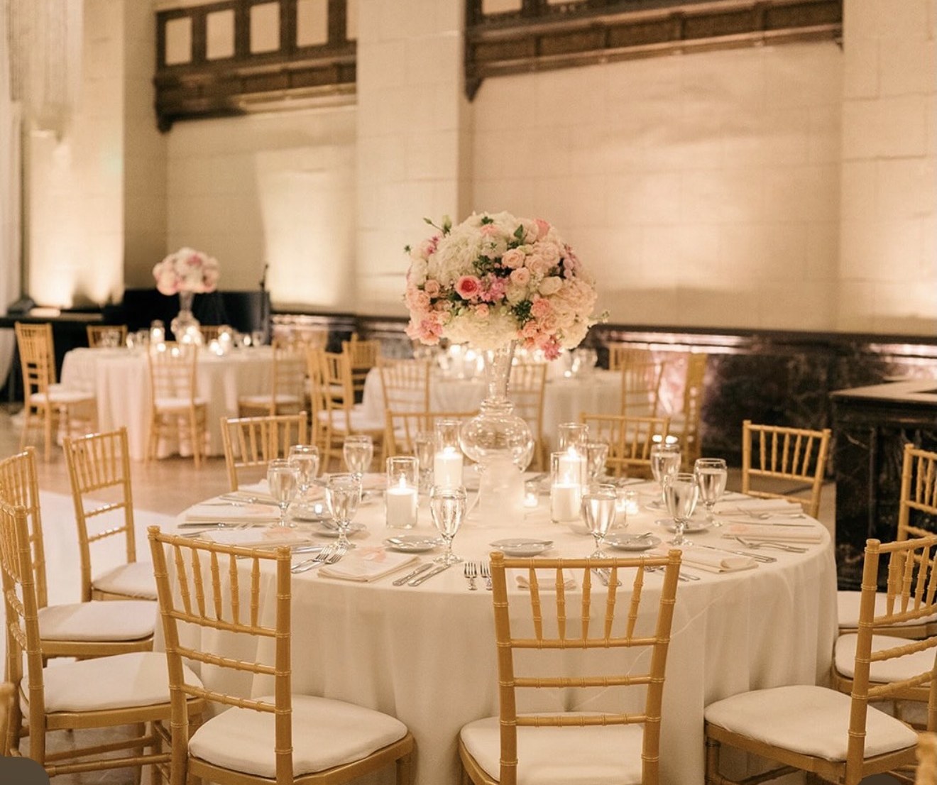Round ballroom table with gold chiavari chairs and a tall blush centerpiece