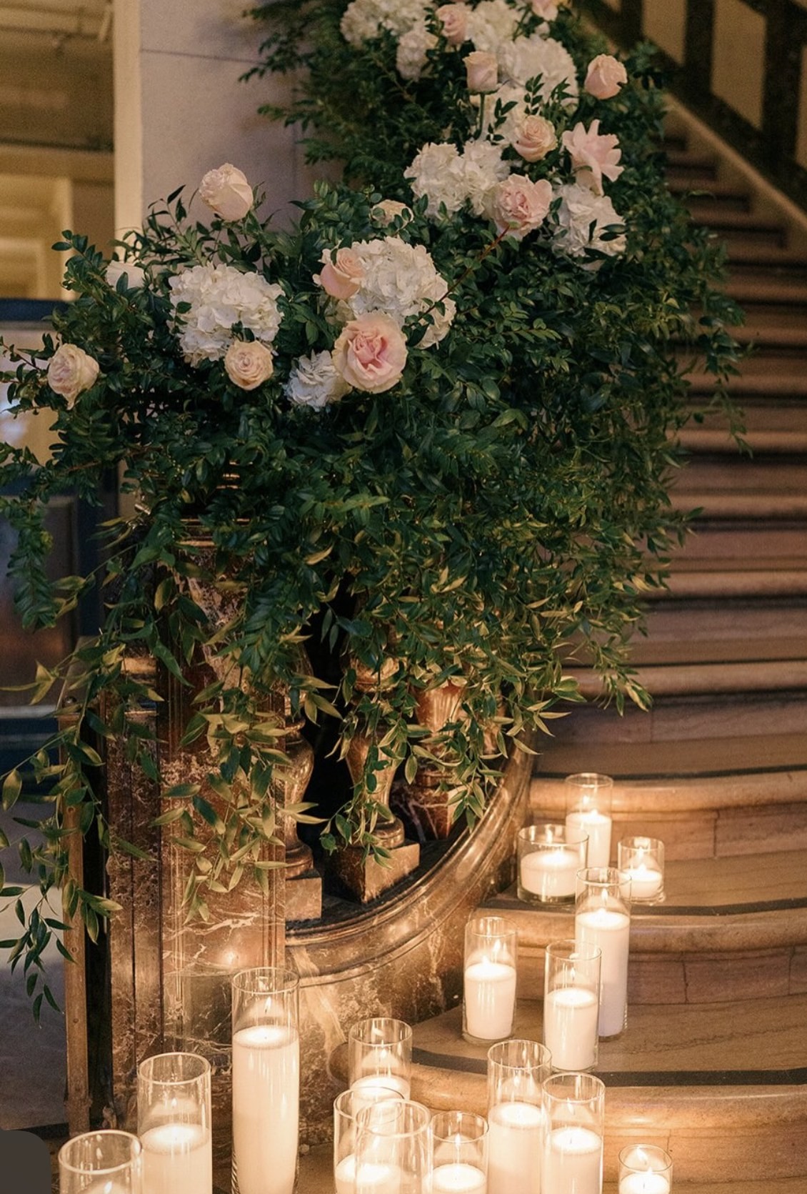 Greenery and rose installation cascading down a staircase lined with candles