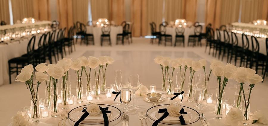 Head table lined with single white roses in glass vases and candles