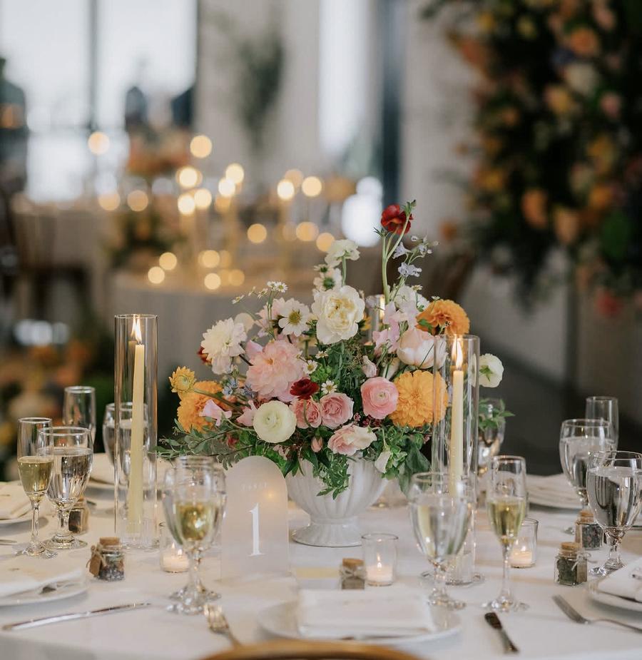 Centerpiece arrangement of peach, white and ivory blooms in a white urn